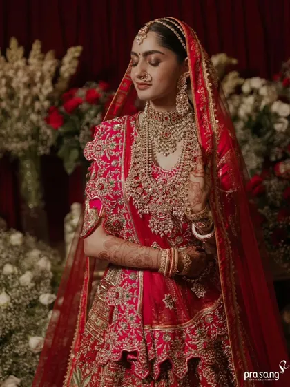 The bride, a vision of royalty. This portrait captures her serene beauty against a rich, red floral backdrop, highlighting the intricate details of her bridal jewelry and attire, all part of the overall aesthetic I curate.