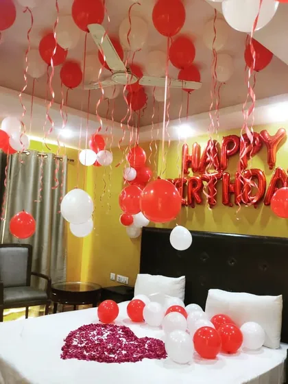 A simple room decoration for a birthday surprise. Red and white balloons on the ceiling and bed, along with a heart made of rose petals, create a classic romantic look.