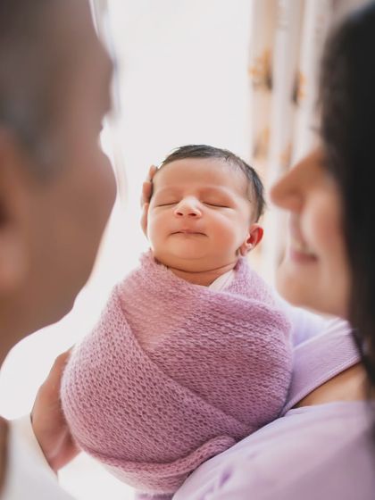 A beautiful family portrait with a newborn. The parents' soft focus in the background keeps the attention on their peacefully sleeping baby.