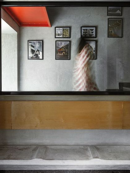 A moment in our studio where a concrete bench is set below a large window looking into a workspace. A bright red ceiling detail and a gallery wall of our project sketches add layers of color and narrative to the space.