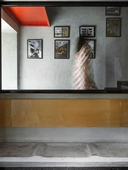 A moment in our studio where a concrete bench is set below a large window looking into a workspace. A bright red ceiling detail and a gallery wall of our project sketches add layers of color and narrative to the space.