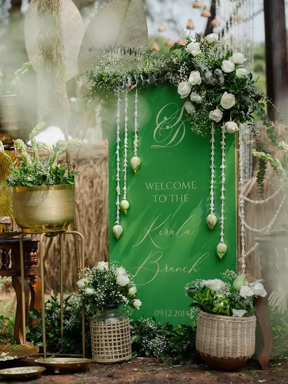 Welcome to the Kerala Brunch. I designed this welcome sign using a rich green, accented with traditional hanging flowers and rustic woven elements, to set the theme for a nature-inspired brunch.