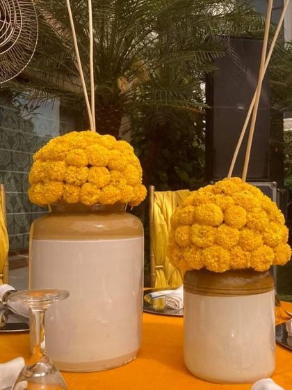 Simple yet elegant table decor for a Mehendi or Haldi lunch. These traditional ceramic jars filled with bright yellow marigolds add a touch of rustic charm to the vibrant setting.