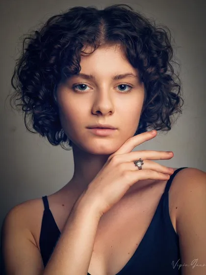 A classic headshot for a model's portfolio. The lighting is designed to accentuate her features and curly hair, while the pose is simple and direct, which is what agencies look for.