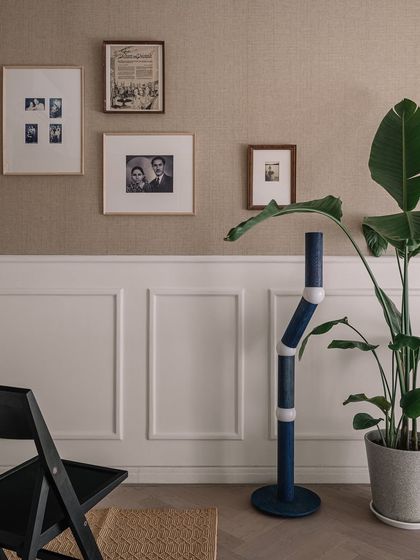 A corner of the den, where family photos and a statement floor lamp create a personal and inviting atmosphere. The combination of jute wallpaper and classic wainscoting adds layers of texture.