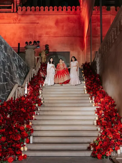 The bride's grand entrance down a staircase lined with dense clusters of red roses and candles. This dramatic floral arrangement created a powerful and romantic welcome.