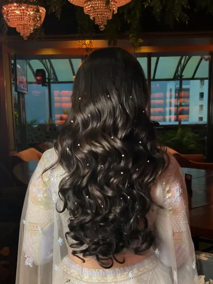 A view of the hairstyle for this reception look. The long, flowing waves are adorned with pearls, adding a touch of romance and sophistication.