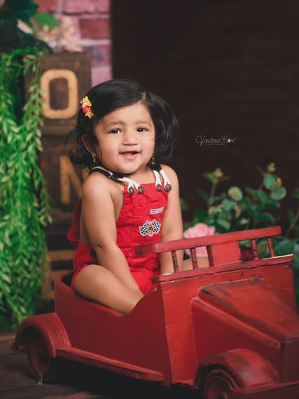 Vroom vroom! This toddler is having a blast in her little red car prop. The rustic wooden backdrop and greenery complete this fun and playful studio setup.