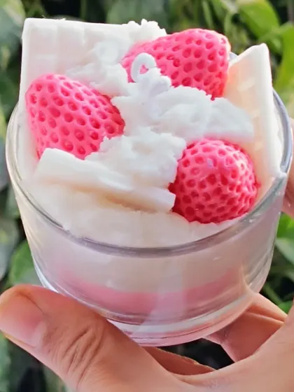This is my strawberry ice cream dessert candle. It features layers of pink and white soy wax, topped with wax strawberries and whipped cream details in a glass cup.