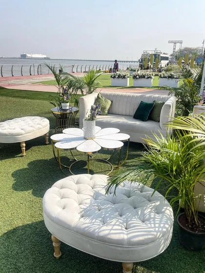 A chic seaside lounge area with modern white furniture and lush green plants. The flower-shaped coffee table adds a playful touch to this clean and sophisticated outdoor setup.