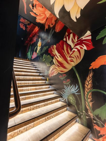 The floral mural continues down the staircase, guiding guests with a river of color. The lit steps highlight the intricate details of the hand-painted tulips, poppies, and wheat.