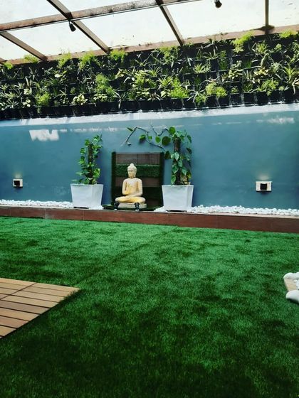 A tranquil balcony garden featuring a Buddha statue, a vertical garden wall, and a lush artificial lawn.