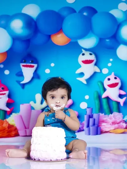 Doo doo doo! A fun and messy cake smash with a Baby Shark theme. This little one is having a blast with his first taste of cake in our colorful underwater studio setup, complete with a balloon arch and friendly shark characters.