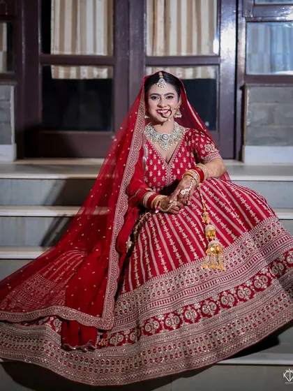 A full-length portrait of the bride seated on the steps, her red lehenga spread beautifully around her. This shot is all about regal elegance.