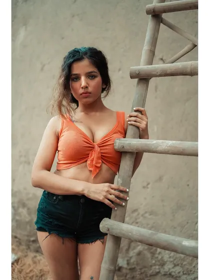 A close-up from the ladder series, where the direct eye contact creates a strong connection. The simple orange top pops against the neutral, textured background.