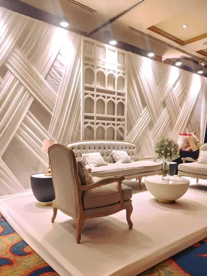 A classy lounge setup in white and beige, perfect for guest conversations. The backdrop features intricate white draping and a traditional jharokha-style panel, blending modern comfort with classic design.