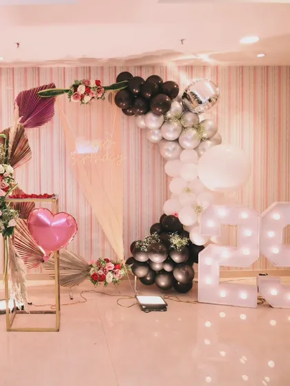 A modern and romantic 29th birthday setup, with a black, white, and silver balloon arch, a personalized photo display, and large marquee numbers.