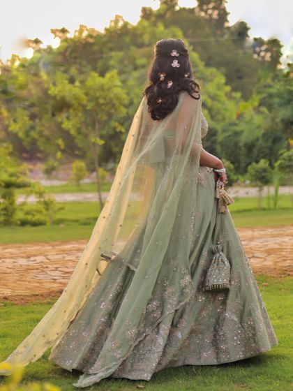 The back of this Matsya World lehenga features a sheer cape, adding a touch of modern drama to the otherwise traditional silhouette. The floral hair accessories complete the look.