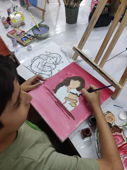 A young boy carefully paints a portrait of a mother and child, using a reference sketch to guide his work during our Mother's Day special session.