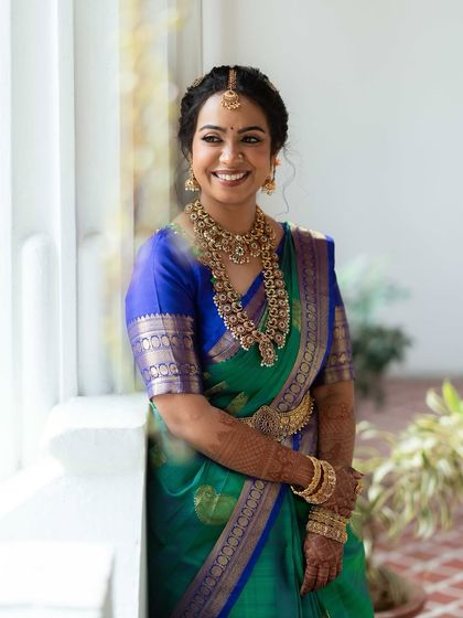 A candid moment of joy. This bride's radiant smile is enhanced by a soft glam makeup look, featuring defined eyes and a natural lip tone that harmonizes with her beautiful green and blue silk saree and antique-finish jewellery.