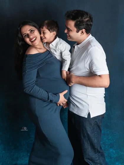 Pure happiness in one photo. The big brother's excitement is contagious in this classic family maternity portrait against a deep blue studio backdrop.