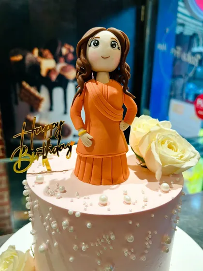 A close-up of a custom fondant figurine of a woman in a traditional orange dress.