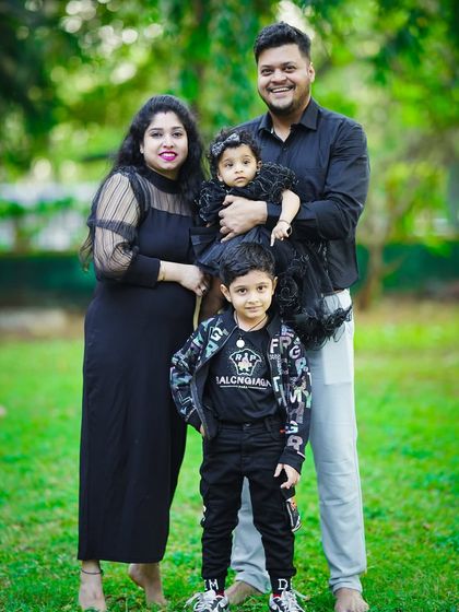 A stylish family of four, dressed in coordinated black outfits, poses for a group portrait in a beautiful green park.
