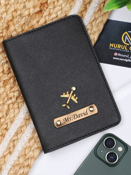 A classic black personalized passport cover with 'Mr. David' and an airplane charm.
