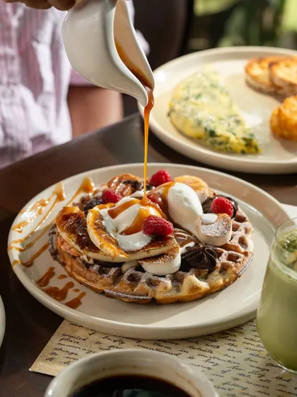 A decadent waffle topped with ice cream, fruit, and caramel sauce. The pouring action adds a sense of indulgence.