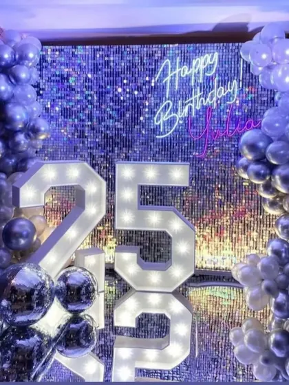 For a milestone 25th birthday, we created this ultra-glam photo corner. The setup features a silver shimmer wall that catches the light beautifully, a custom neon sign, and oversized marquee numbers, all framed by a cascade of metallic balloons.