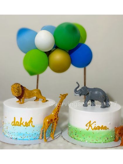 Celebrating twins with this elegant jungle-themed cake set. Each cake features a different animal friend, like a lion, giraffe, and elephant, with balloon toppers.
