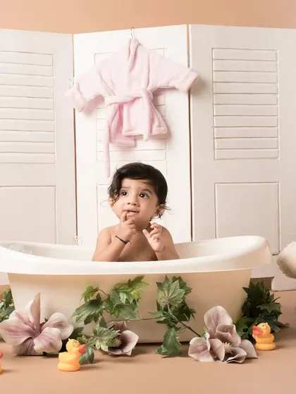 A thoughtful moment during a bathtub-themed shoot. The setup includes a vintage-style tub, floral decorations, and rubber ducks, creating a sweet and whimsical scene for a sitter session.