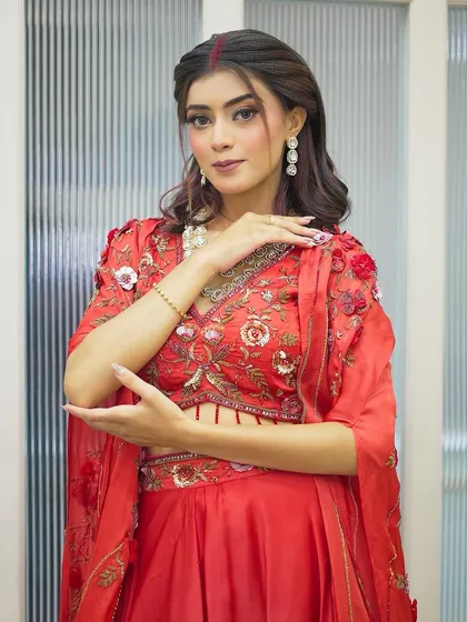 A client dressed in a beautiful red outfit for Karva Chauth. Her makeup is traditional yet glamorous, with a focus on radiant skin and defined eyes.