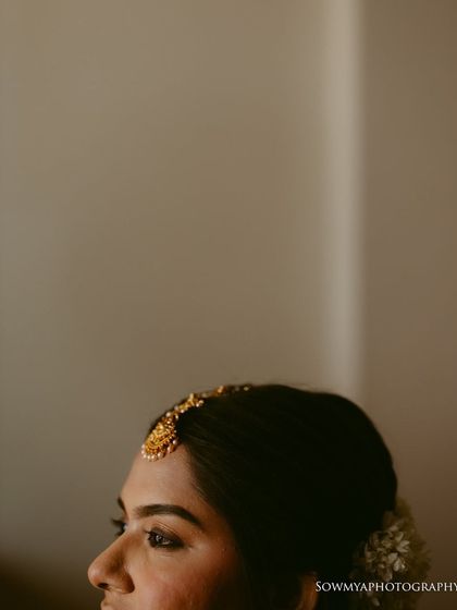 A close-up, artistic shot focusing on the bride's maang tikka and profile. The soft, minimal focus creates a dreamy and thoughtful mood.
