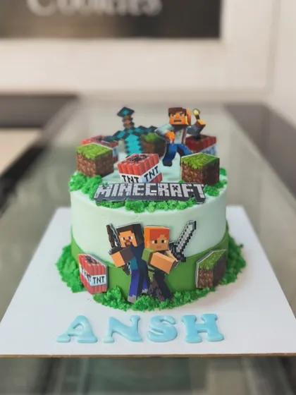 An action-packed Minecraft world built entirely from cake for a young gamer's birthday. This custom video game themed cake features edible characters, TNT blocks, and grassy terrain, all 100% eggless.