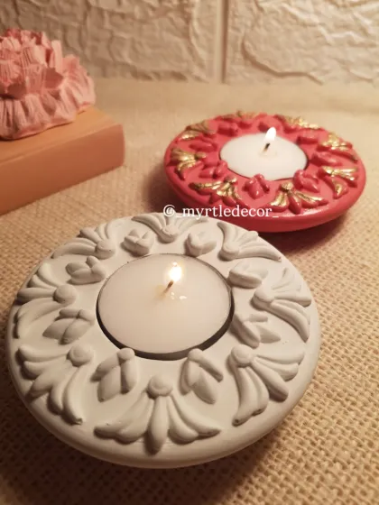 Two of our ornate Jesmonite T-light holders, with their flames lit. The design is inspired by traditional motifs, and they cast a beautiful, warm light perfect for Diwali or any celebration.