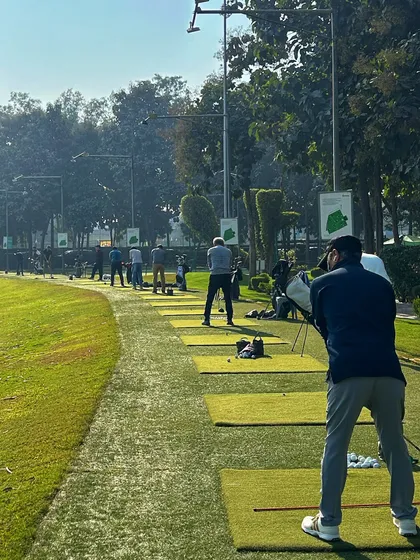 A view from behind a golfer as he watches his shot, looking down a long line of fellow players.