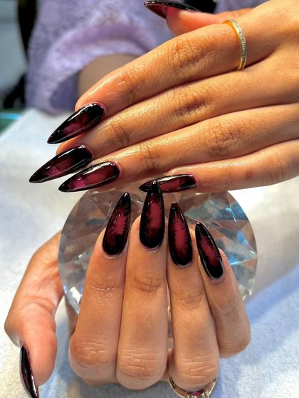 Dark and fierce with a touch of glam. These long, sharp stiletto nails feature a black and red ombré design for a dramatic, vampy look.
