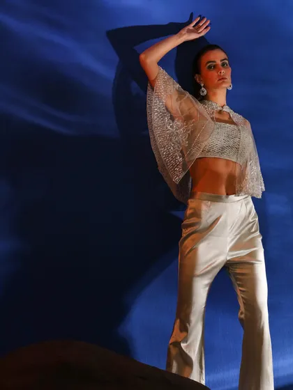 This shot uses a projected blue wave pattern as a backdrop, creating an underwater feel. The model wears a sheer, embellished capelet, and the pose is strong and statuesque.