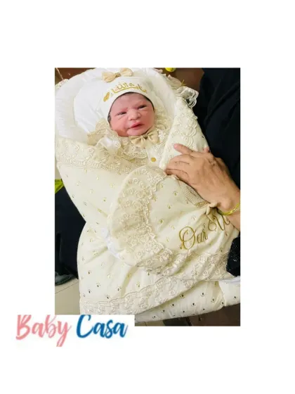 Fresh from the hospital and wrapped in love. This newborn girl is nestled in a cream and gold lace trimmed wrap, personalized with the words "Our Wish," a truly heartfelt welcome.