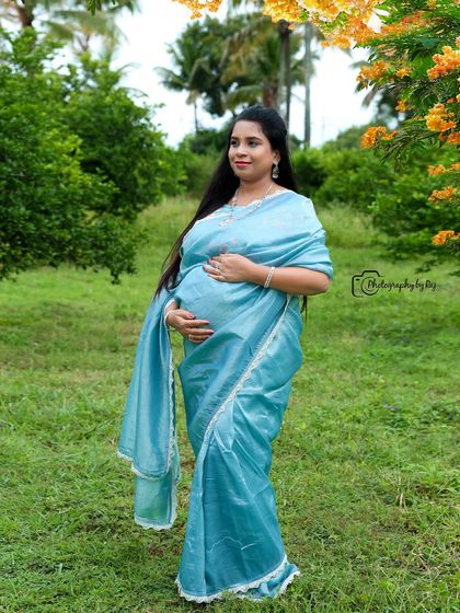 A solo portrait of a mother-to-be in a light blue saree, standing in our lush garden. The long, flowing pallu adds a touch of drama.