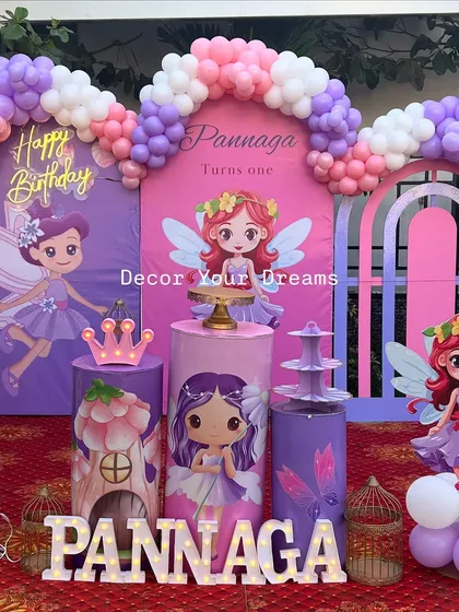 A magical first birthday with a fairy theme, perfect for an outdoor celebration. This setup includes a custom backdrop, a multi-colored organic balloon arch, character cutouts, and themed plinths for the cake and desserts.