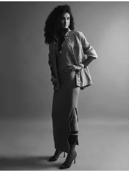 A powerful black and white full-length studio portrait. The strong composition and classic monochrome tones highlight the layered styling of a denim jacket over a long dress, demonstrating a timeless approach to fashion portraiture.