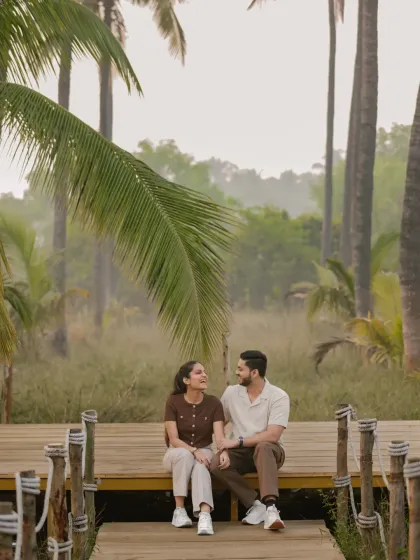 A lovely, composed shot of Vinay and Yachi sitting on a wooden deck. The framing with the large palm leaf adds a natural, tropical feel to this quiet, conversational moment.