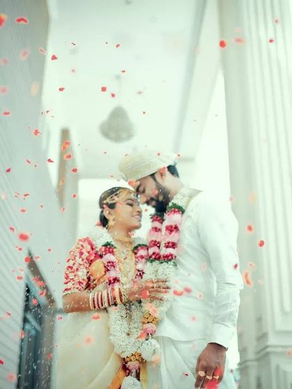 A beautifully framed shot of a couple in all-white wedding attire, surrounded by a shower of red petals.