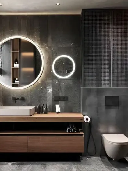 A modern bathroom design that uses dark tiles and wood textures to create a moody, spa-like feel. The backlit circular mirror and floating vanity add a touch of elegance and make the space feel larger.