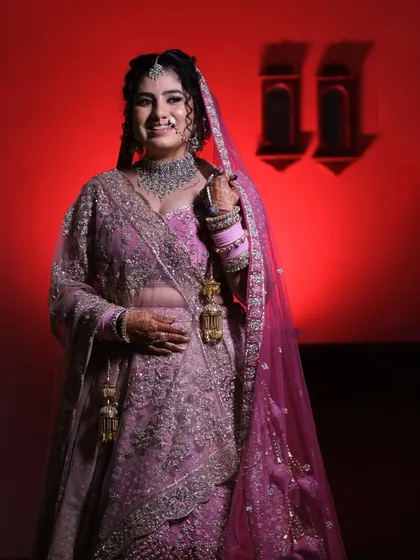 A vision in pink against a bold red background. This bridal portrait captures the bride's joyful smile and the stunning details of her wedding lehenga.