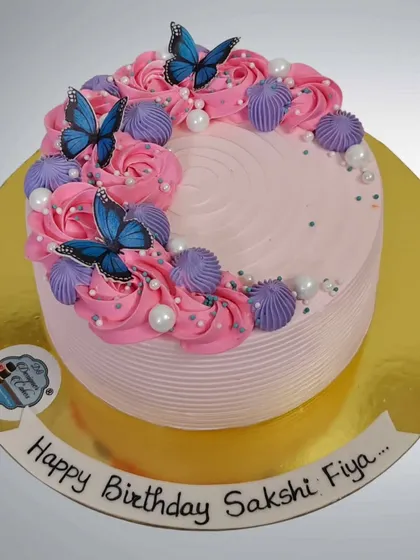 A pretty pink birthday cake decorated with blue butterflies and piped rosettes. The combination of colors creates a vibrant and cheerful design.