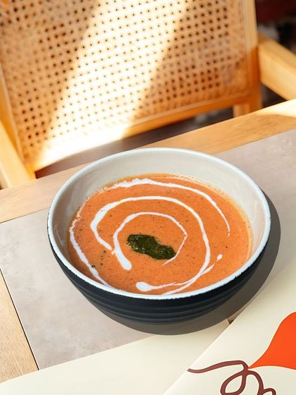 A comforting bowl of our creamy tomato soup, swirled with fresh cream and topped with a basil leaf. It's simple, classic, and delicious.