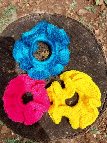 A trio of my vibrant crochet scrunchies in blue, pink, and yellow, pictured in a natural outdoor setting.